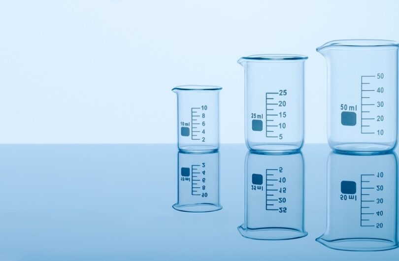 Three,Empty,Measuring,Beakers,Sitting,On,A,Mirror,Blue,Surface,
