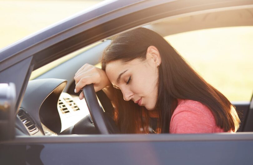 Transportation concept. Tired beautiful woman driver has sleepy expression, stop on road as can`t drive any more, wants to have rest, leans at wheel, poses in car, feels overworked and fatigue